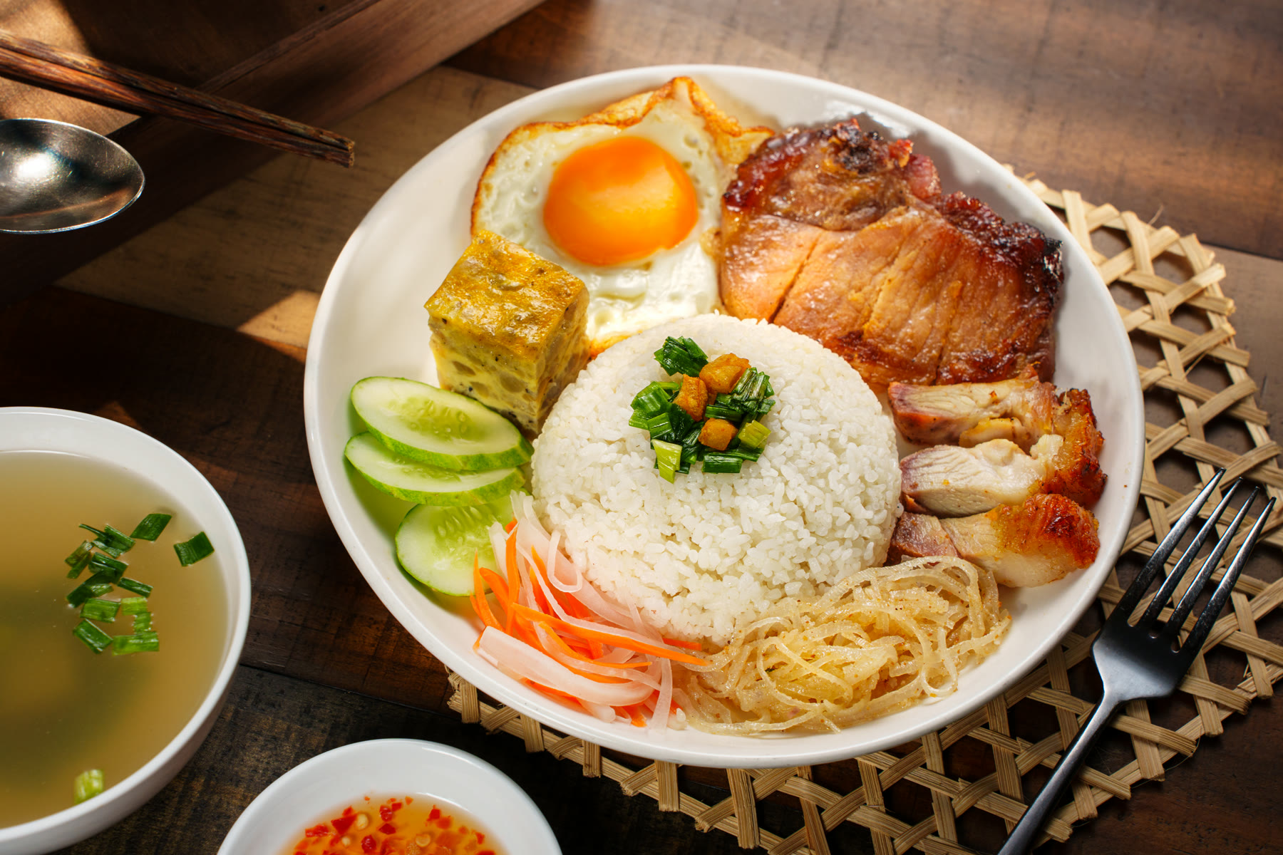 Grilled pork and chicken rice plate with a fried egg, cucumber and pickled carrot