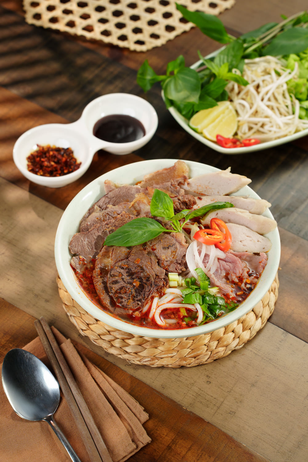 A bowl of bún bò Huế with sliced beef, fresh basil and chilli, served with dipping sauces