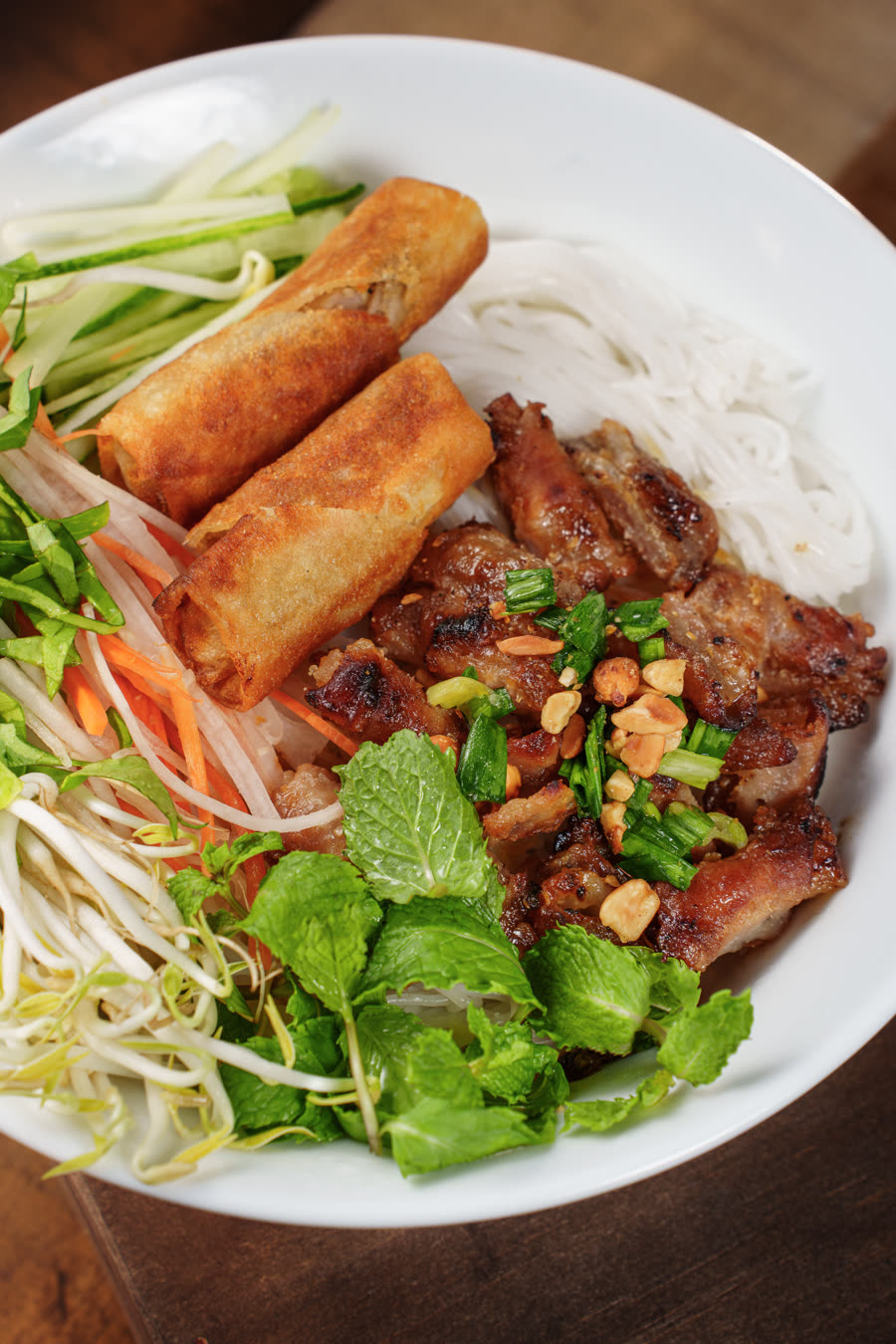 Vermicelli bowl with char-grilled pork, spring rolls, fresh herbs and crushed peanuts