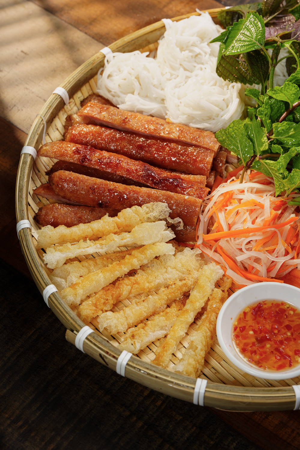 Grilled pork, crispy rice-paper sticks, vermicelli and fresh herbs on a bamboo sharing tray
